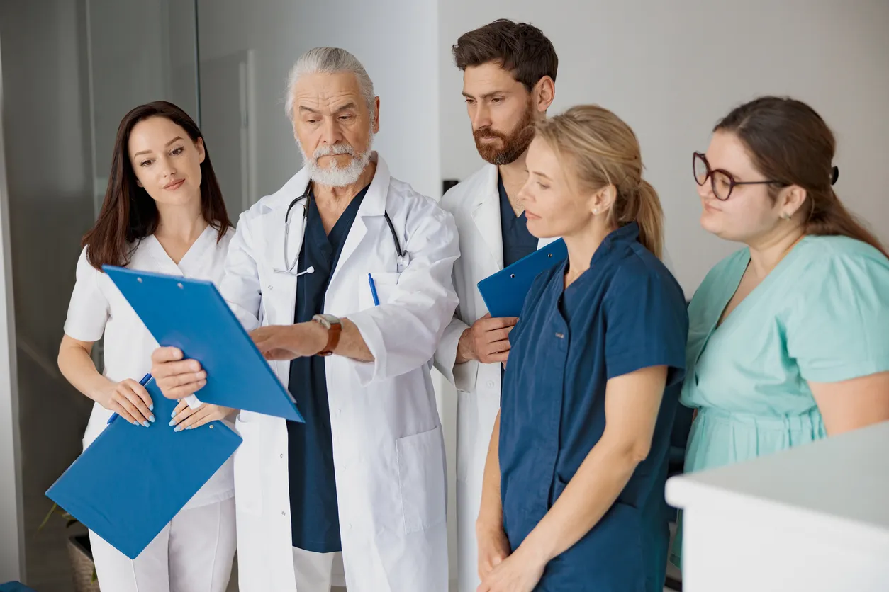 Médico impartiendo una diagnostico de un paciente a internos con uniformes de varios colores en el hospital