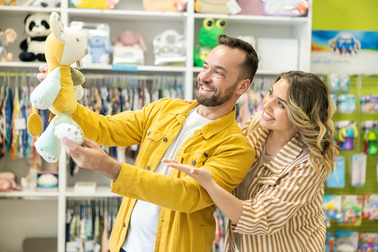 Una alegre pareja explora y disfruta de su tiempo mientras compra productos para bebés en un animado ambiente comercial.