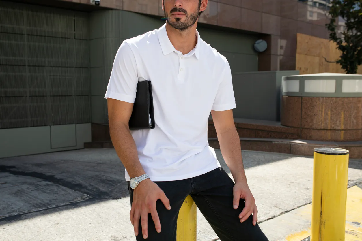 Hombre joven con playera slim fit hombre color blanca recargado en un tubo de estacionamiento.y carpeta en su brazo