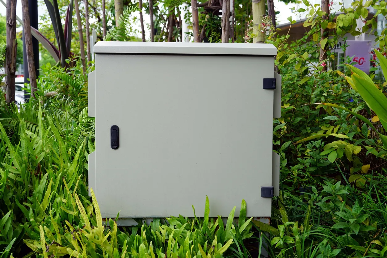 Vista frontal de una caja eléctrica gris en el césped del jardín.