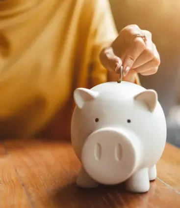 Mano de una persona colocando una moneda en una alcancia representando el ahorro para el retiro