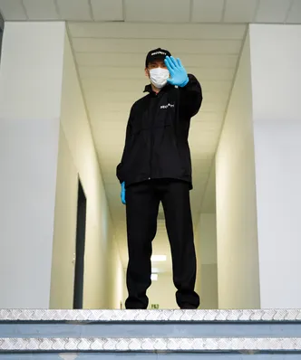 Hombre de seguridad privada con uniforme azul marca el alto con su mano en el pasillo de un edificio